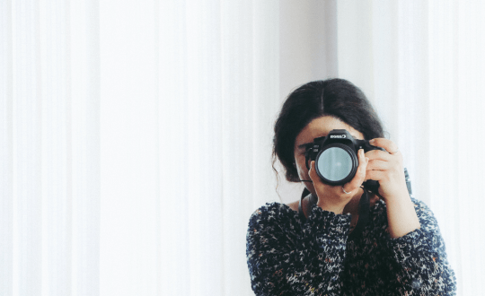 Girl in sweater taking a photo with a professional camera.