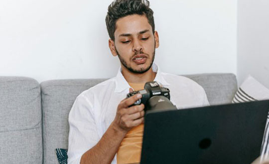 Man with camera sitting on couch using laptop.