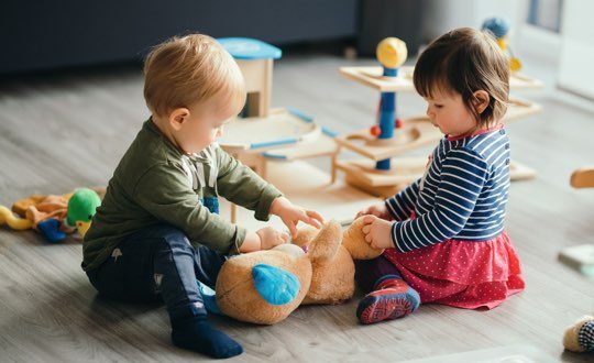 Two toddlers playing with a stuffed animal.