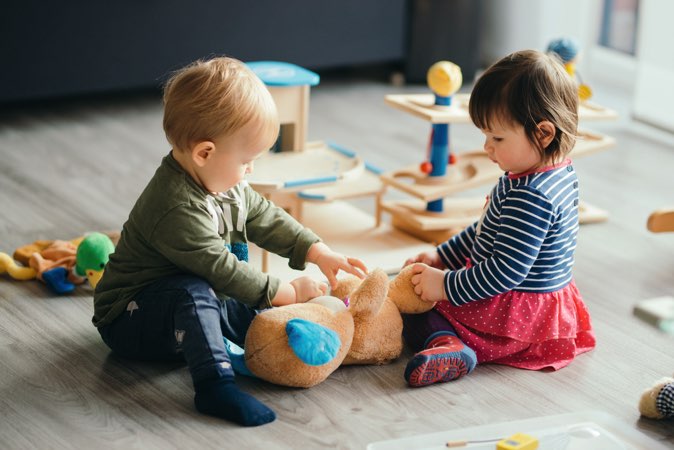 Two toddlers playing with a stuffed animal.